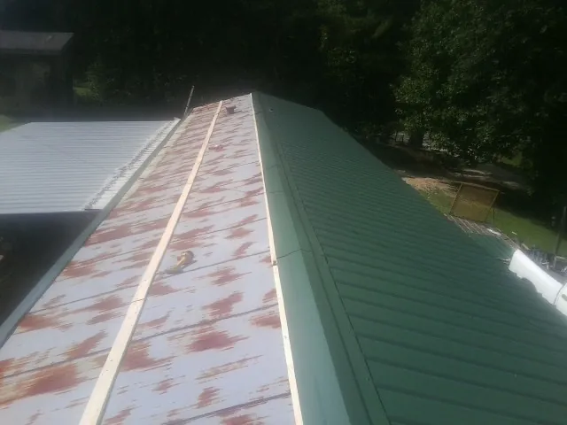 Old rusted panels beside newly installed green metal roofing — Wind Damage Roof Repair by Roofing Brothers in Williamson