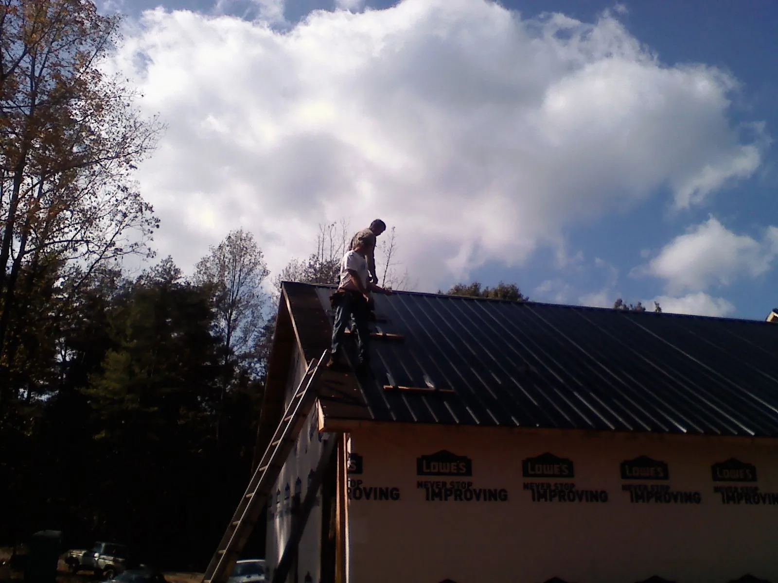 Roofer fastening dark metal panels high against a cloudy sky, from a Roof Inspection job in Williamson