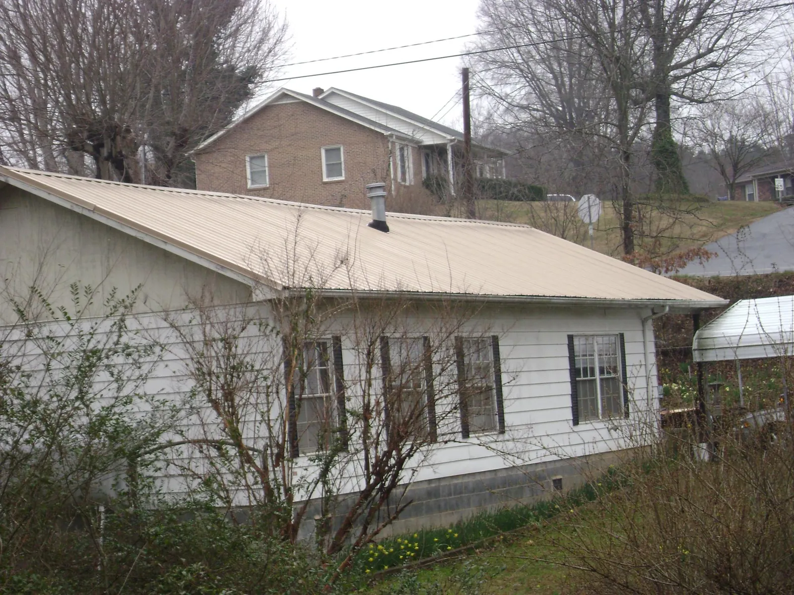 Tan metal roof on a white sided house set into a hillside — Commercial Roofing by Roofing Brothers in Williamson